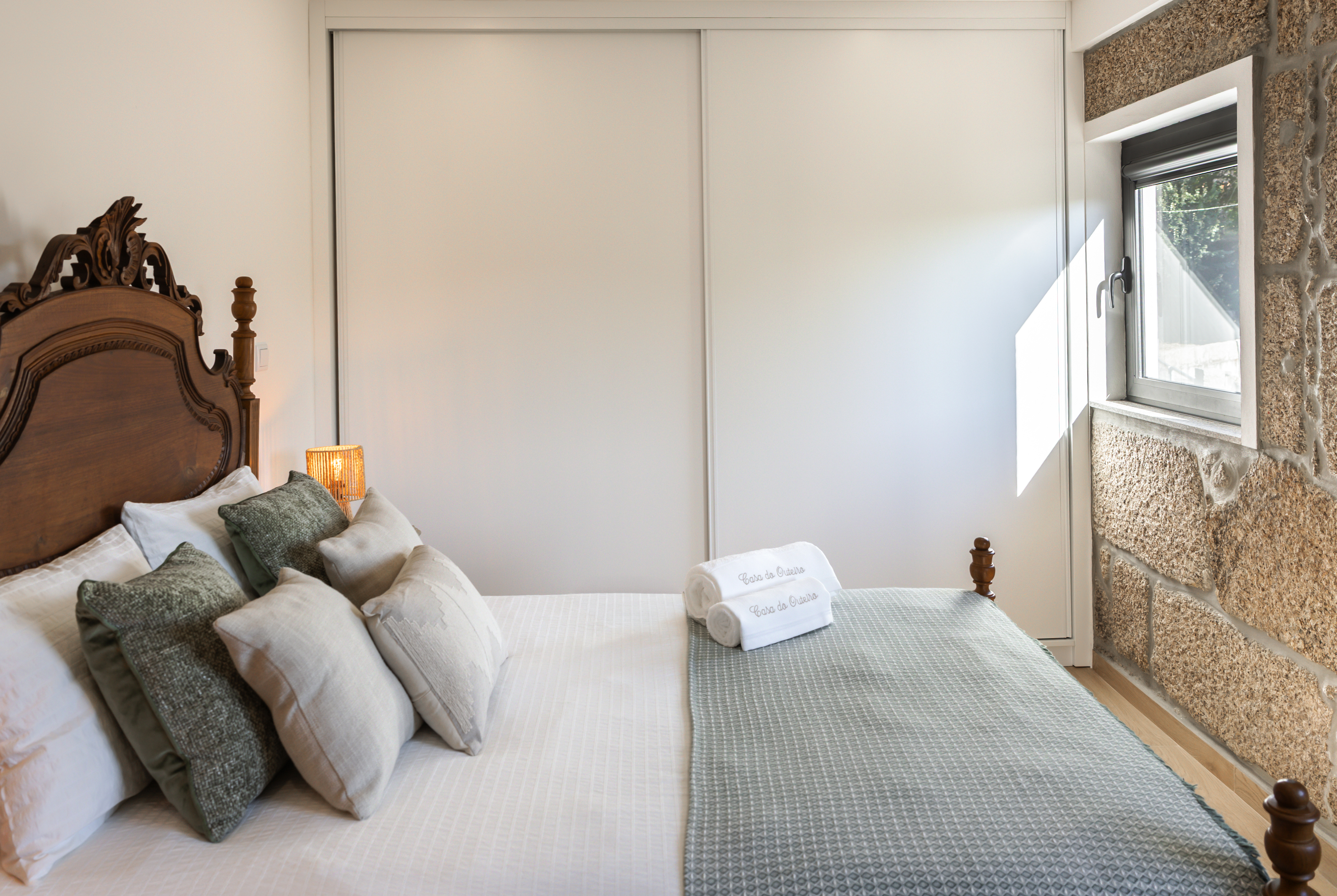 Quarto com cama de casal, cabeceira em madeira antiga e parede em granito à vista